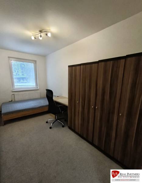 A room in a 4-room apartment with a bed, table, chair, and wardrobe on a carpet.