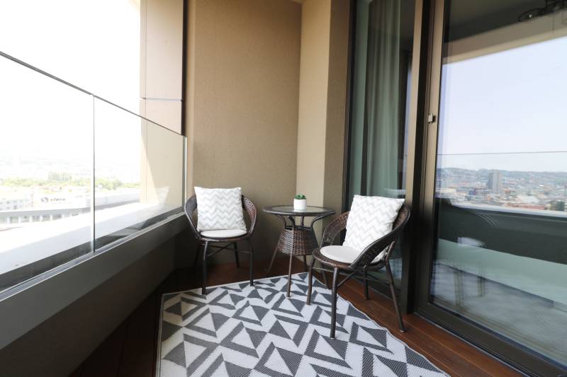 A balcony in a 2-room apartment with rattan furniture and a view of the city.