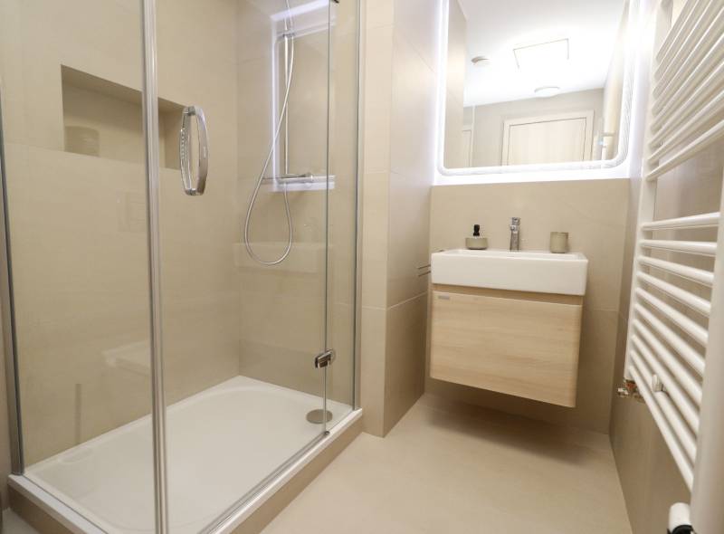 A bathroom with a glass shower enclosure and a light-colored sink in a 2-room apartment.
