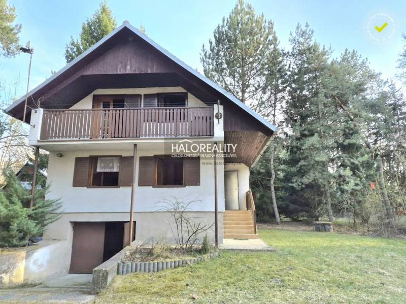 A cottage in Borský Svätý Jur surrounded by greenery and trees, with a wooden balcony.