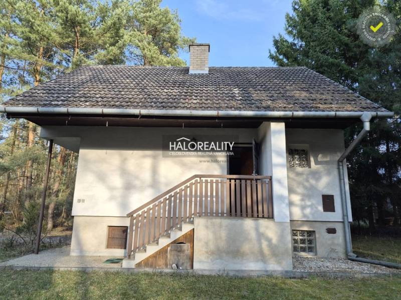 A cottage in Borský Svätý Jur in the middle of the forest with a balcony and a sloped roof.