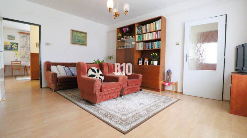 Living room of a family house with a sofa, armchairs, and a bookshelf on a floor with a wooden decor.