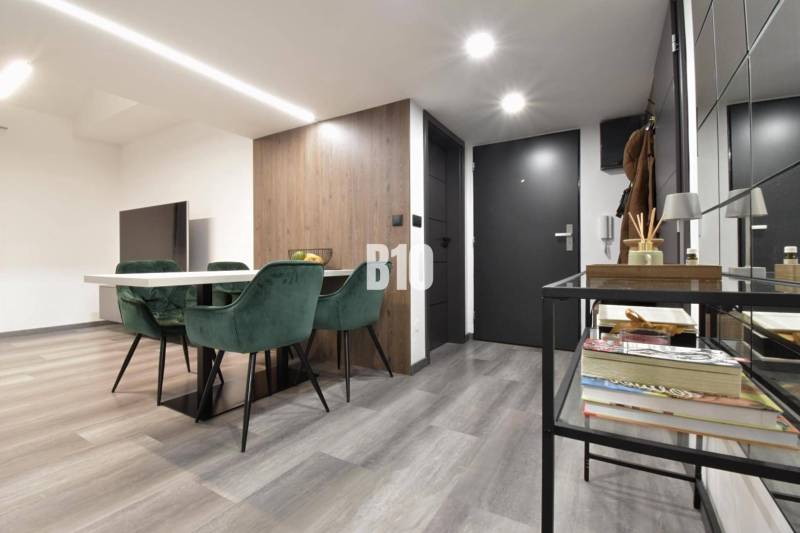 Interior of a 4-room apartment with a wooden decor floor, dining table, and green chairs.