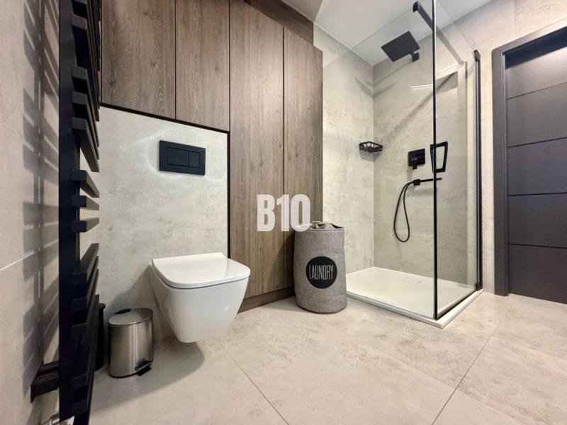 Bathroom in a 4-room apartment with a toilet, shower, and floor with wood decor.