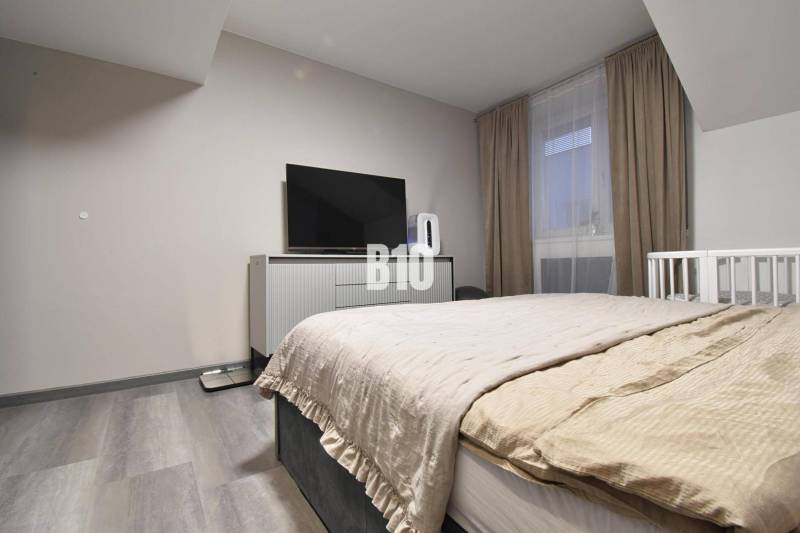 Bedroom in a 4-room apartment with a TV, bed, and wooden decor flooring.