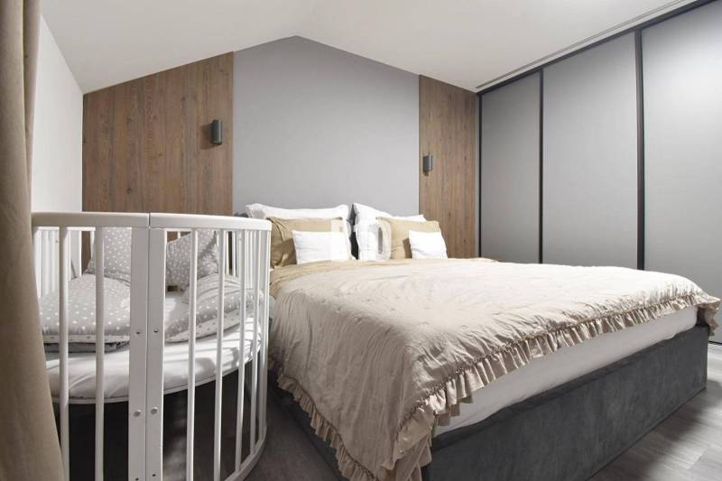 A bedroom with a bed, a baby crib, wooden decor, and neutral colors in a 4-room apartment.