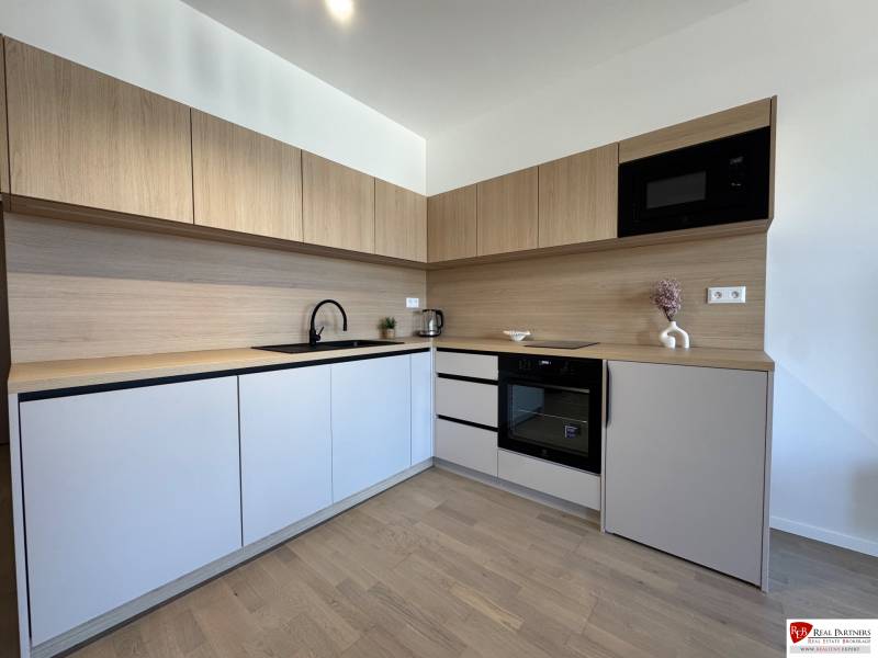 A kitchen in a studio apartment with a wood-patterned floor, wooden cabinets, and appliances.