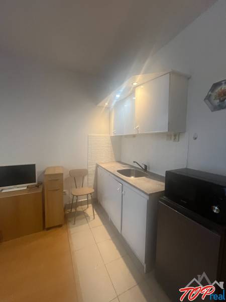 Kitchen corner in a studio apartment with a microwave, refrigerator, and chair.