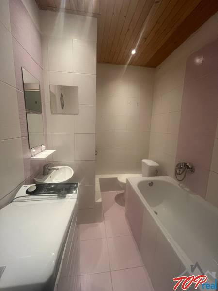 A bathroom in a studio apartment with a bathtub, washing machine, sink, and toilet.