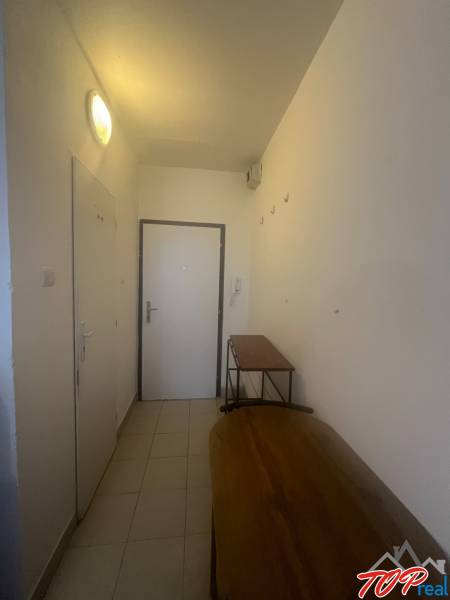 A narrow hallway in a studio apartment with simple furniture and white walls.