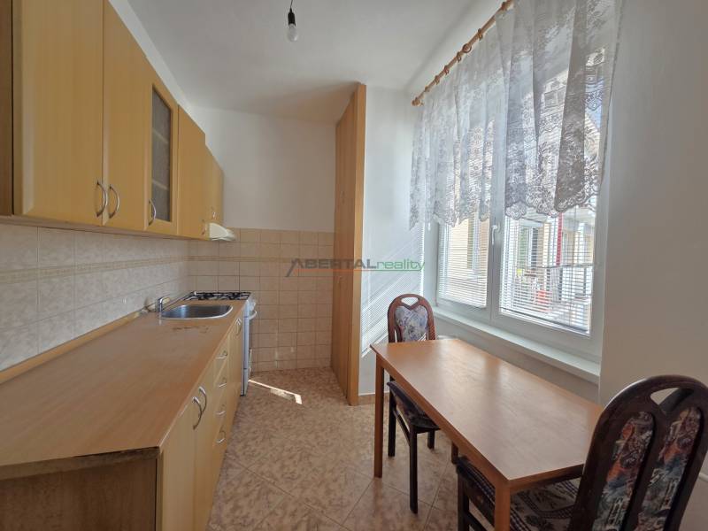 A kitchen with wooden cabinets, a table, and two chairs in a three-room apartment.