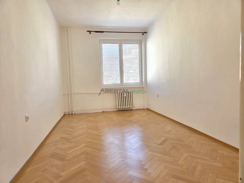 An empty room with a wood-patterned floor in a 3-room apartment, bright walls, radiator.