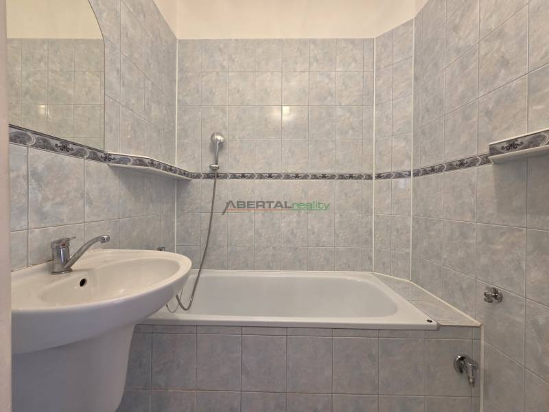 A bathroom with a bathtub in a 3-room apartment, tiled with light ceramic tiles.