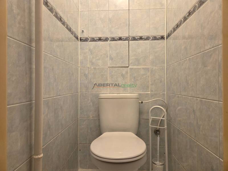A toilet with white ceramic tiles in a 3-room apartment.