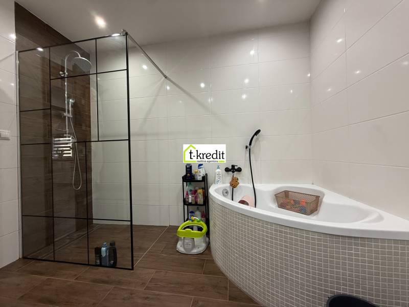 A bathroom in a family house with a corner bathtub and a shower, flooring with a wooden decor.