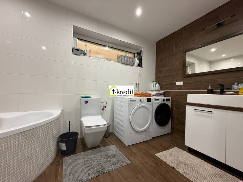 A bathroom in a family house with a bathtub, washing machine, dryer, and a floor with a wooden decor.