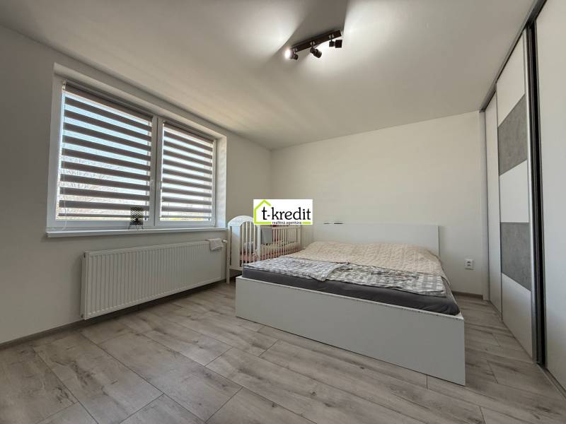 A bright bedroom in a family house with a bed, a wardrobe, and a wooden-patterned floor.