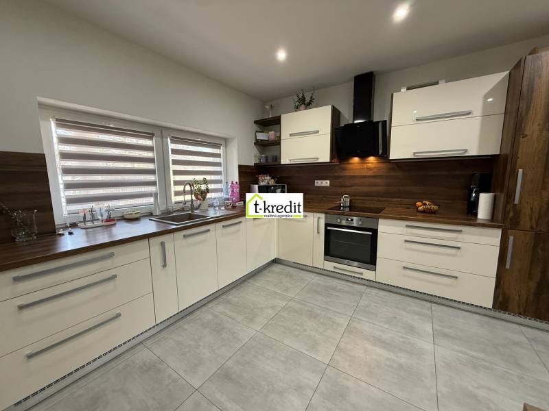 A kitchen in a family house with large windows and built-in appliances, flooring with a wooden decor.
