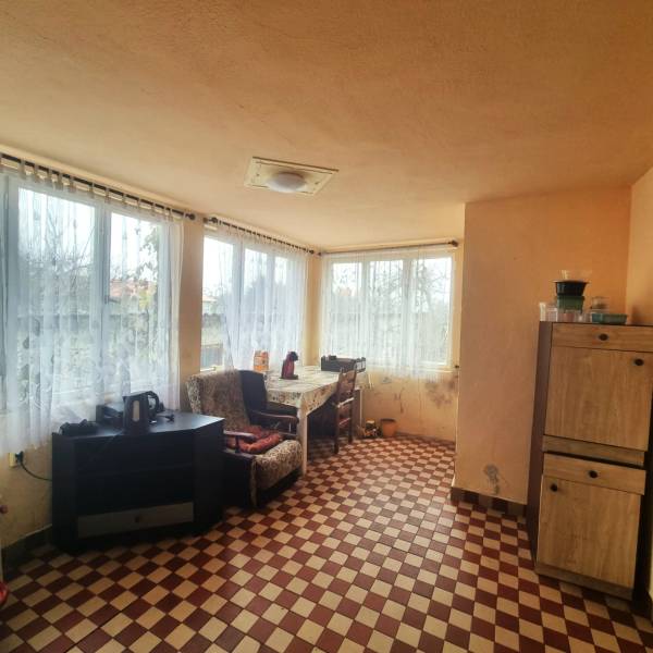 A room in a family house with a checkered floor, furniture, and large windows with a view.