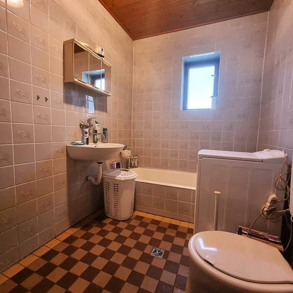 A bathroom in a family house with a bathtub, sink, and washing machine, checkered tiles.