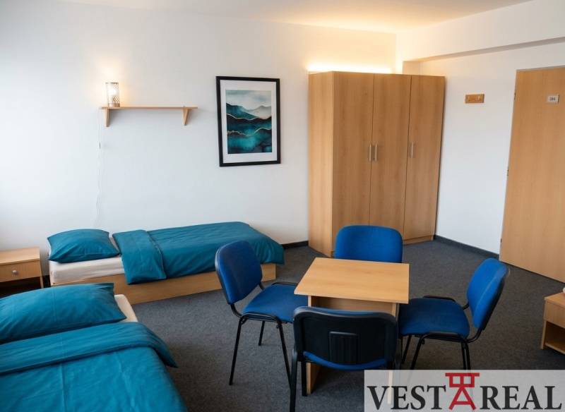 A room with two beds, blue bed linen, a wardrobe, a table, and four chairs.