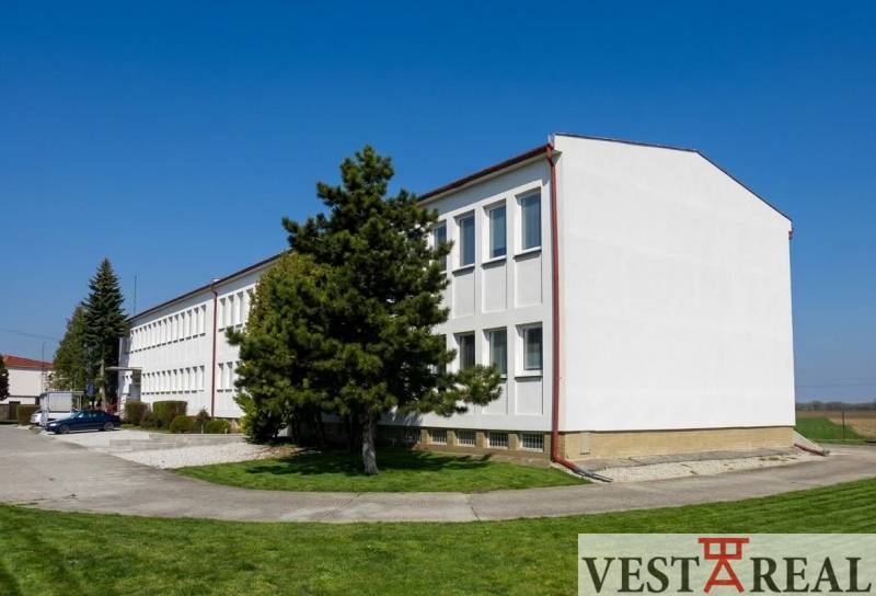 A building in Šoporňa surrounded by greenery and trees, with a clear blue sky.
