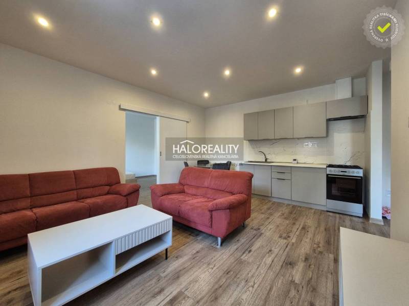 Living room in a two-room apartment with a wooden decor floor, red sofas, kitchen.
