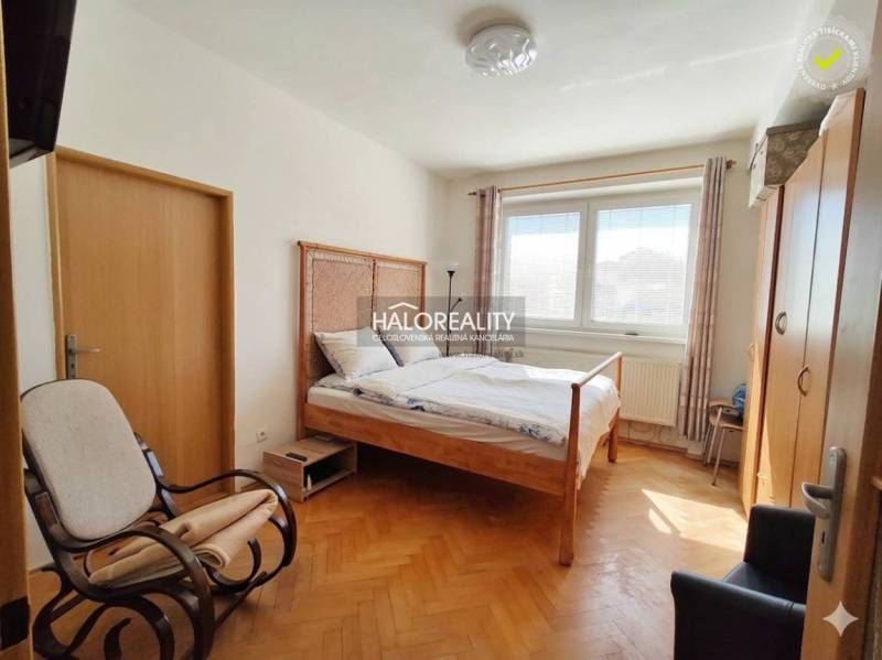A room in a 3-room apartment with a bed, a table, a wooden decor floor, and yellow walls.