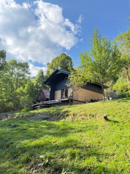 A cottage in Horná Mariková surrounded by green trees on a sunny slope under a blue sky.