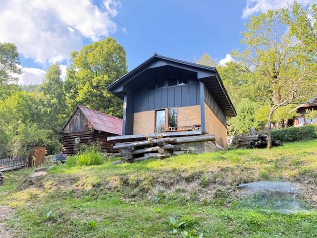 A cottage in Horná Mariková, surrounded by nature and wooden structures, on a sunny day.