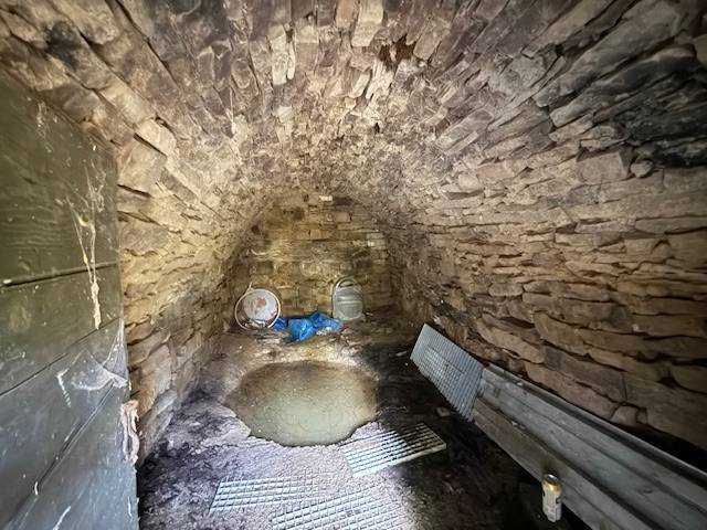A stone cellar of a cottage with a vaulted ceiling and metal accessories.