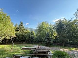 Nature in Horná Mariková with a cottage, a table with benches surrounded by trees and mountains.