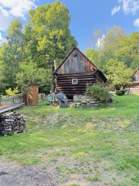 A wooden cabin in Horná Mariková surrounded by greenery and stacks of wood.