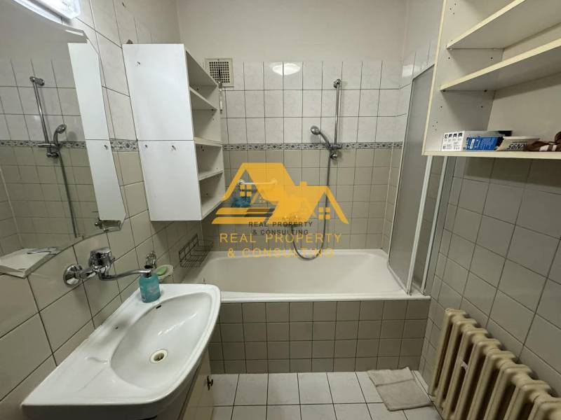 Bathroom with a bathtub, sink, white cabinets, and a radiator in a family house.