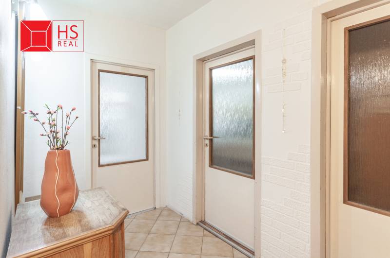 A hallway in a 3-room apartment with a flower on a wooden table and a door with glass.