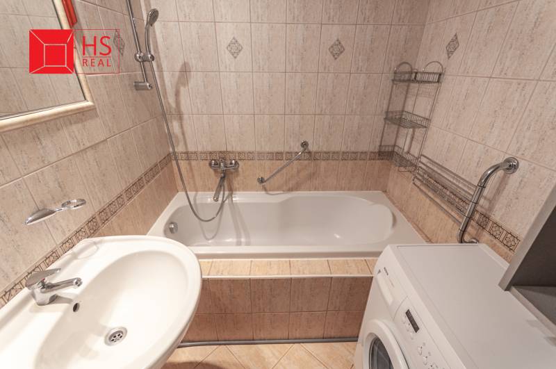 A bathroom in a 3-room apartment with tiles, a bathtub, and a washing machine.