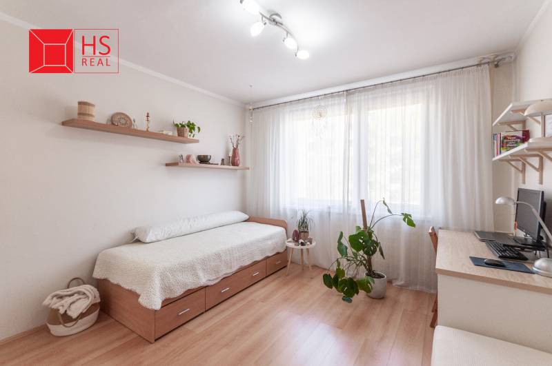 A bright room with a bed, a desk, and a wooden floor in a three-room apartment.