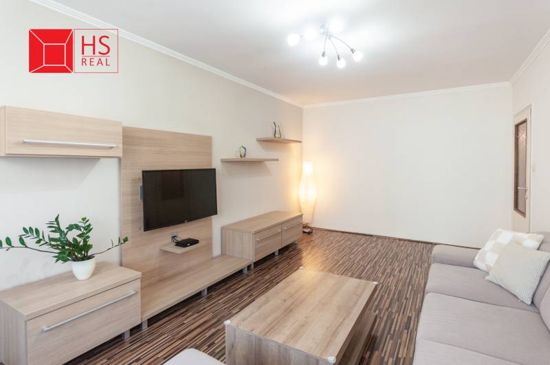 Living room of a three-room apartment with a wooden decor floor and a gray sofa.