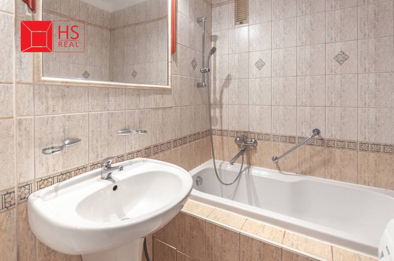 A bathroom in a 3-room apartment with a bathtub, tiles, and a sink, complemented by a mirror.
