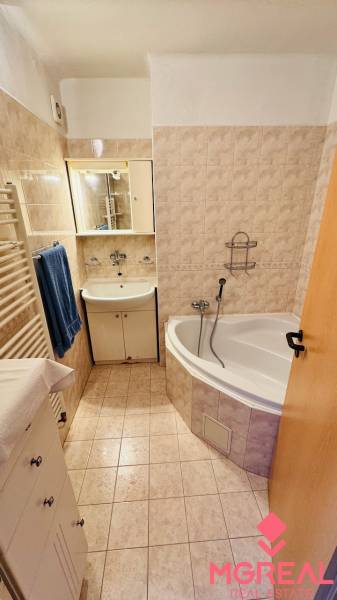 Bathroom of a 3-room apartment with a bathtub, sink, and beige tiles.
