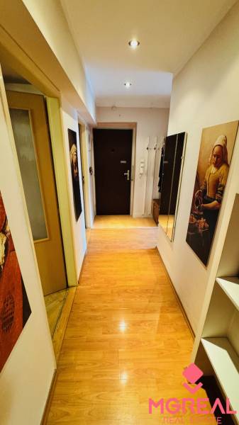 A narrow hallway with a wooden decor floor in a 3-room apartment, with paintings and a mirror.