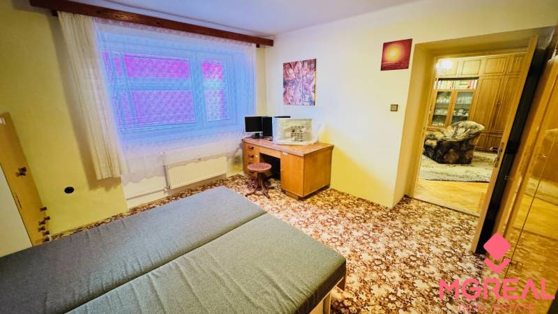 A room in a 3-room apartment with a carpet, a desk, and a bed.