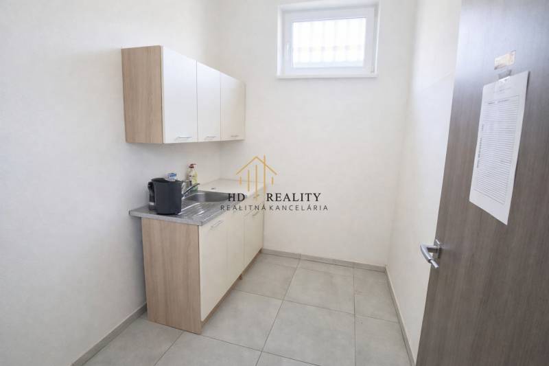 A kitchenette with a sink and cabinets in commercial premises, light tiles.
