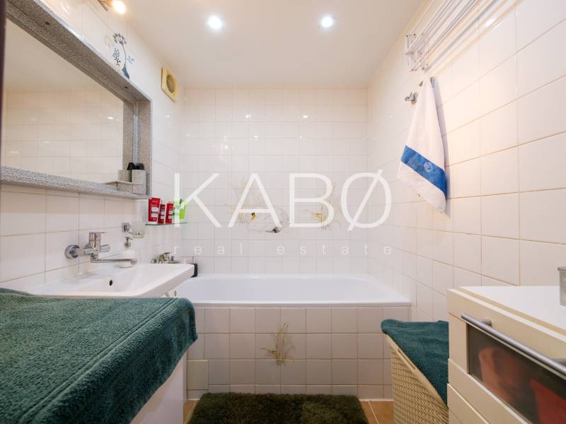 Bathroom in a 3-room apartment with a bathtub, sink, white tiles, and a green carpet.