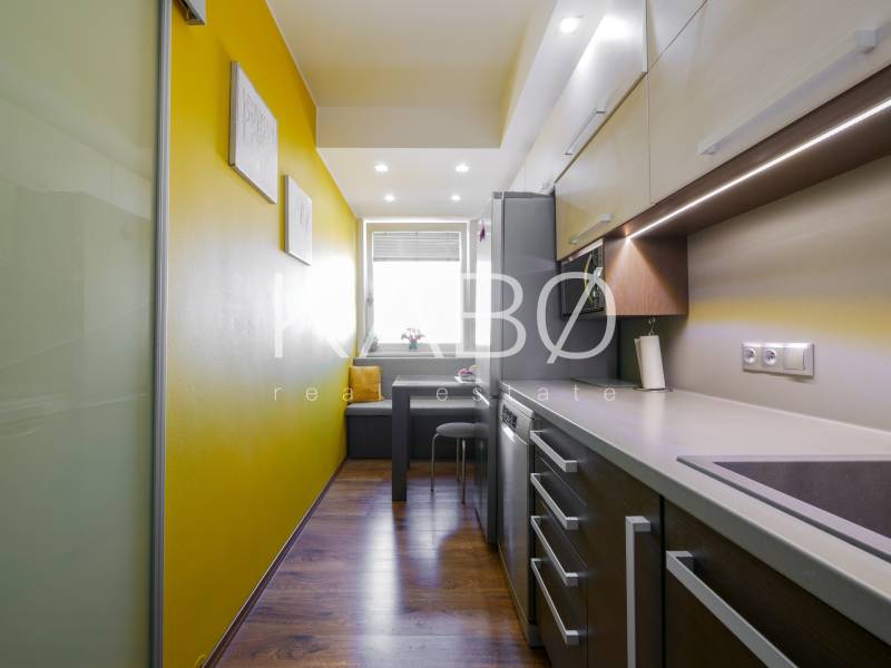 A kitchen in a 3-room apartment with a wooden decor floor and yellow walls.