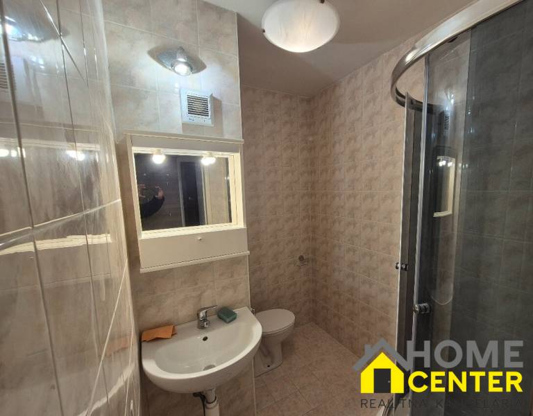 Bathroom with a shower, sink, and light tiles in a studio apartment.