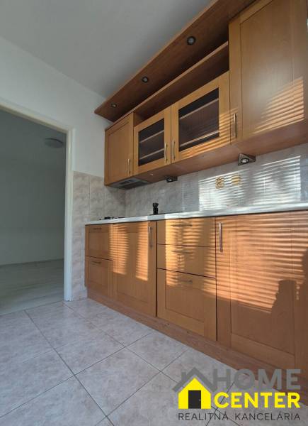 A kitchen unit in a studio apartment with tiles and cabinets with a wood decor.