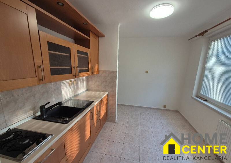 A kitchen in a studio apartment with light cabinets and ceramic tiles.
