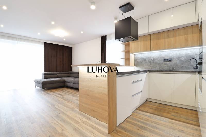 Interior of a 3-room apartment with a kitchen, sofa, and wooden decor flooring.