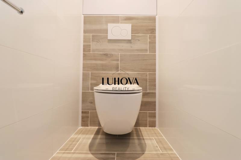A toilet with wooden decor and white tiles in a 3-room apartment.